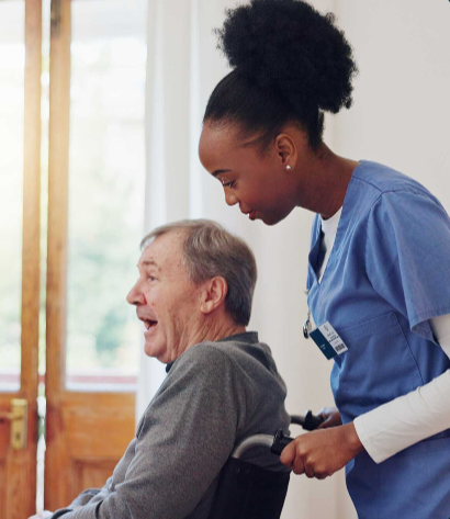 A Chriswell nurse smiling warmly beside an older man in a wheelchair in a bright, sunlit room at home.